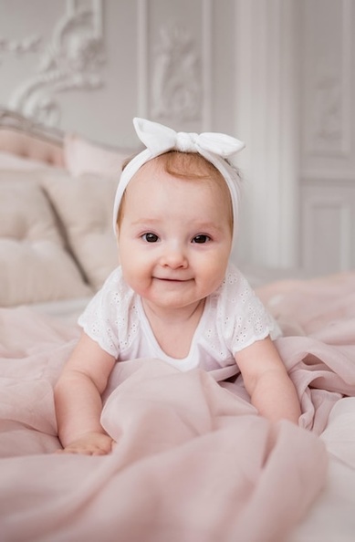 caucasian-little-girl-white-dress-headband-crawls-bed-room-looks-camera_208700-4288.jpg